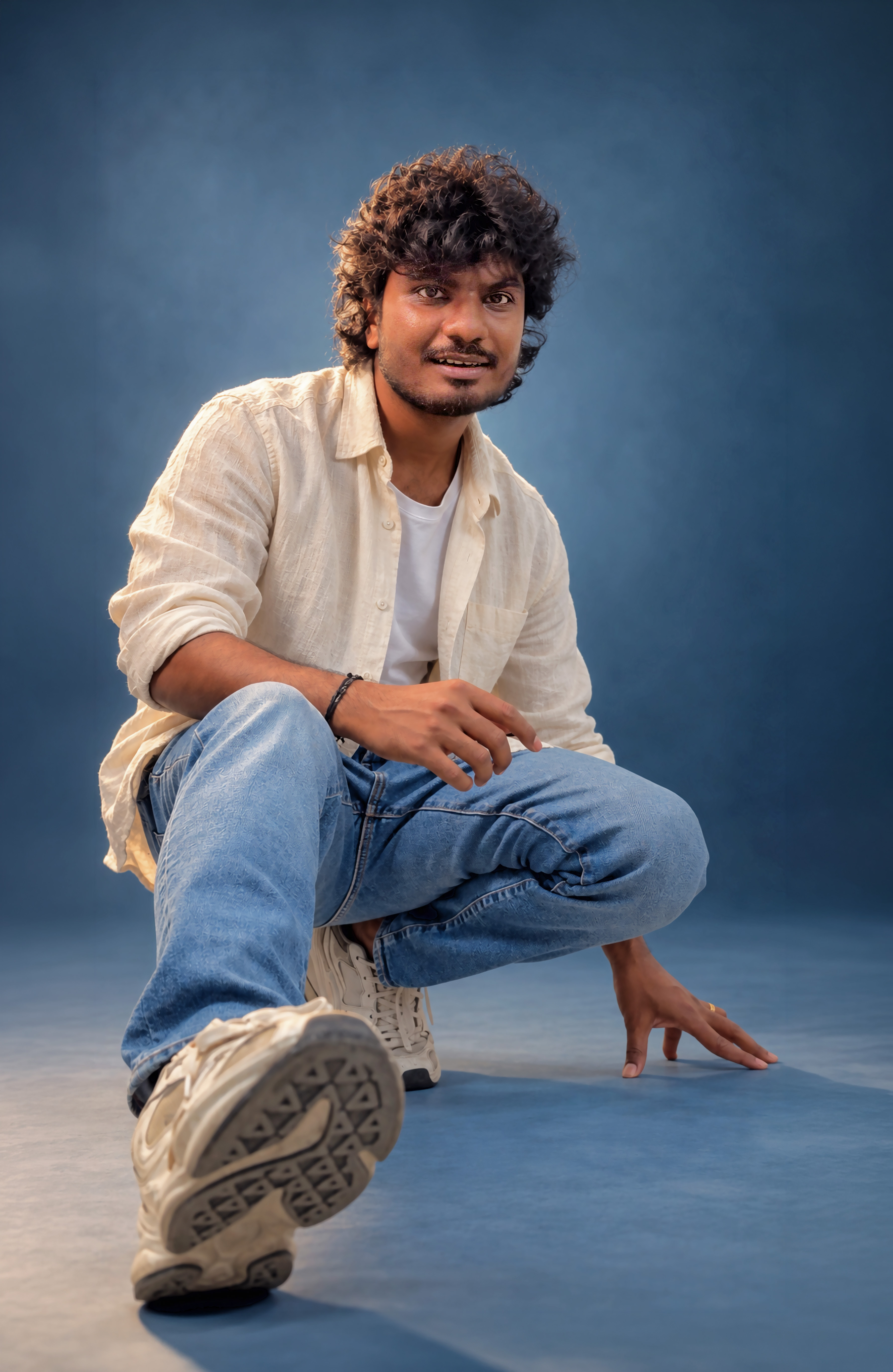 Crouching low in a cream linen shirt and jeans, one hand on the studio floor